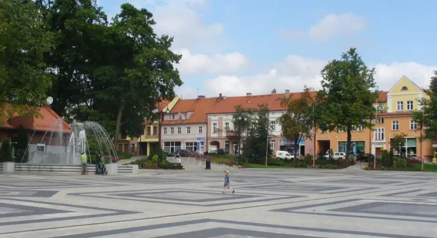 Dziecko biega po placu z fontanną, otoczonym kamienicami. To największy rynek w Polsce, tętniący życiem.