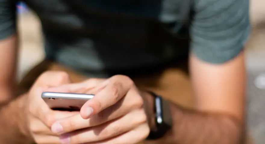 Mężczyzna trzyma smartfon, a na jego nadgarstku widać smartwatch. Właśnie sprawdza, jak sparować zegarek z telefonem.