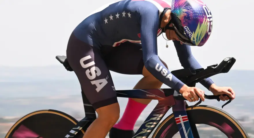 Chloé Dygert, in her USA cycling kit, races against the clock, her focus intense as she powers her bike uphill.