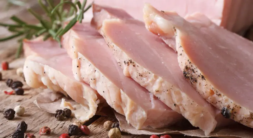 Super delikatny i soczysty schab gotowany, pokrojony w plastry, z gałązką rozmarynu i ziarnami pieprzu.