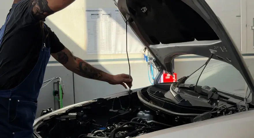 Meccanico con tatuaggi controlla il motore. Capire la differenza tra tagliando e revisione è fondamentale per la manutenzione dell'auto.