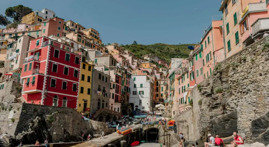 Colorful buildings cling to a hillside overlooking a harbor, a picturesque scene after a train from Bologna to Cinque Terre.