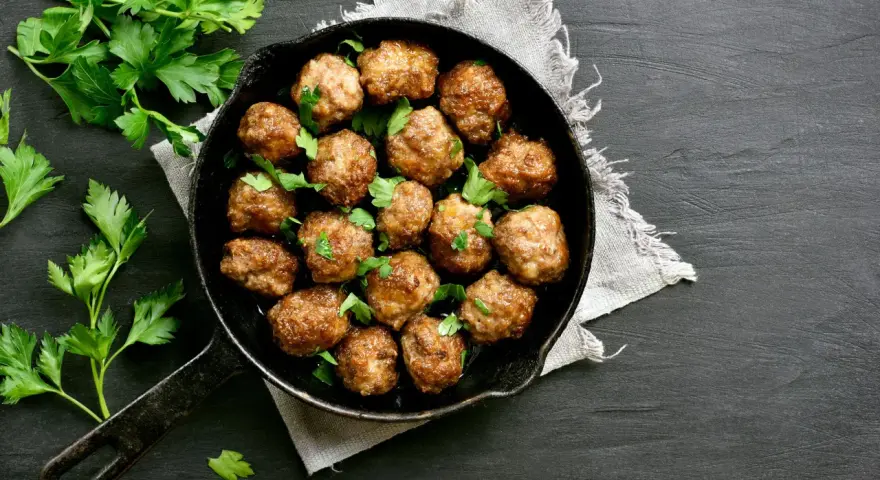 Polpette al forno dorate e succulente, guarnite con prezzemolo fresco, in una padella di ghisa su sfondo scuro.