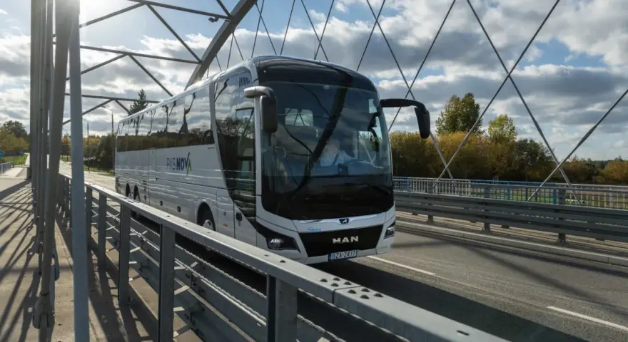 Biały autokar PKS NOVA jedzie przez most, pokonując trasę Warszawa-Augustów.