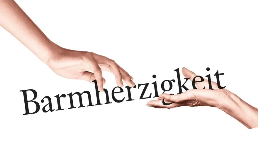 Zwei Hände berühren das Wort "Barmherzigkeit". Eine Hand reicht es der anderen, ein Symbol für die Werke der Barmherzigkeit.