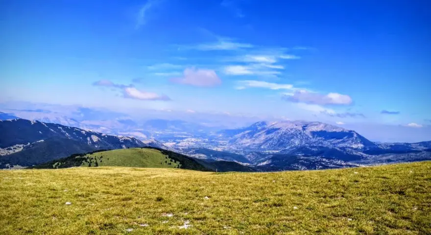 Prato verdeggiante con vista panoramica sul monte Pizzalto e le montagne circostanti sotto un cielo azzurro con nuvole sparse.