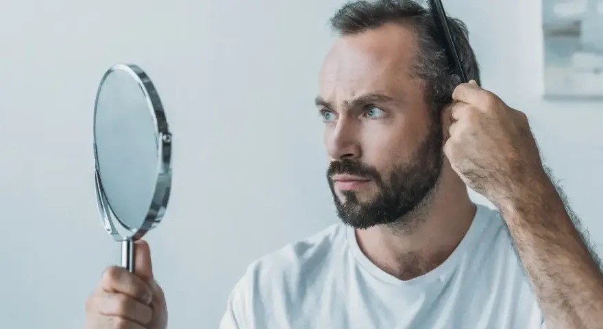 Mann kämmt sich die Haare, besorgt über Haarausfall. Er fragt sich, warum seine Haare nicht mehr wachsen, Frau.