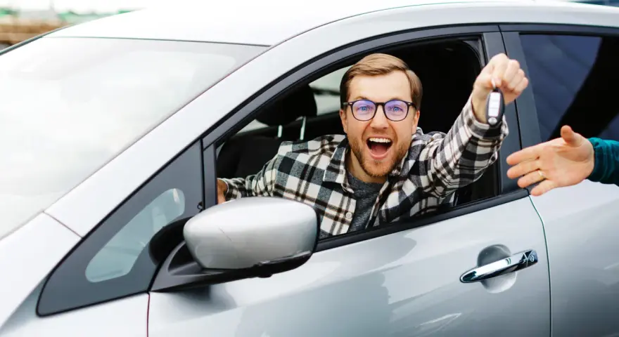 Mężczyzna w okularach wysiada z samochodu, trzymając kluczyki i podając je innej osobie.