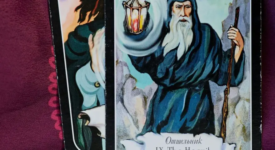 El tarot del mundo ermitaño: un sabio anciano con barba blanca ilumina el camino con una linterna, guiando en la introspección.
