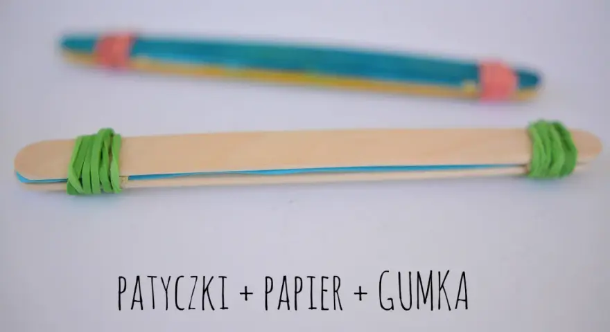 Proste instrumenty muzyczne do zrobienia: patyczki, papier i gumka. Dwa patyczki połączone gumkami, jeden z kolorowym papierem w środku.