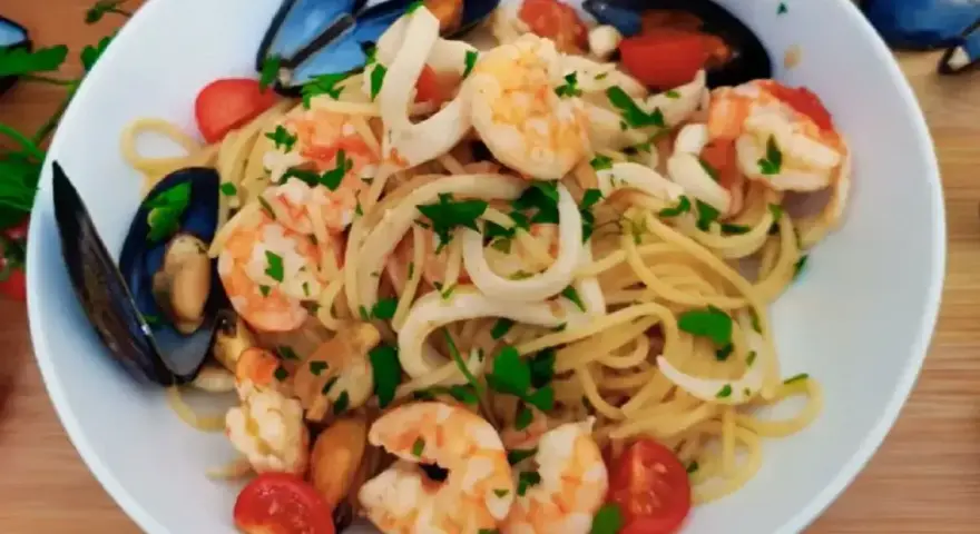 Pyszne linguini z krewetkami, kalmarami i małżami, ozdobione pomidorkami i natką pietruszki.