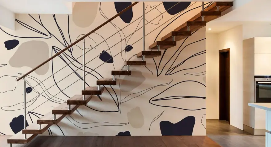 El papel pintado en las paredes de esta casa moderna presenta un diseño abstracto de hojas y formas orgánicas en tonos tierra, complementando la escalera flotante de madera.