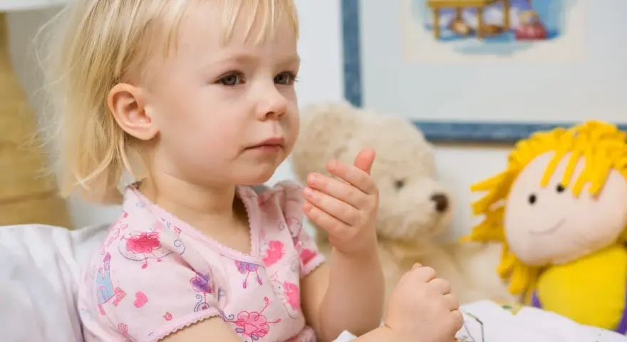 Mała dziewczynka w łóżku, otoczona pluszakami, może mieć zapalenie oskrzeli objawy.