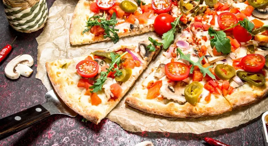 Kawałki pizzy z pomidorkami, jalapeno i rukolą na papierze do pieczenia.