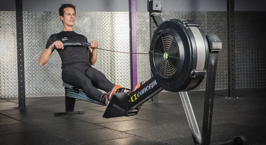 Un homme en tenue de sport effectue un exercice rameur dans une salle de sport.