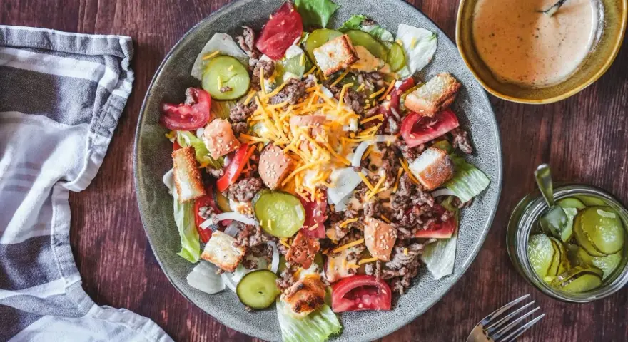 Ein Big Mac Salat mit Hackfleisch, Käse, Tomaten, Gurken und Croutons. Dazu eine cremige Sauce und eingelegte Gurken.