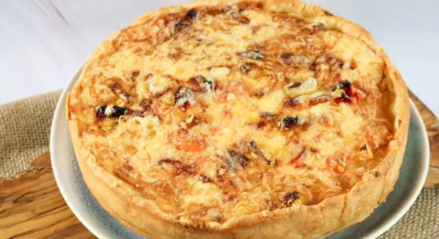 Eine goldbraune Sommer Quiche mit geschmolzenem Käse und bunten Gemüsestückchen, bereit zum Genießen.