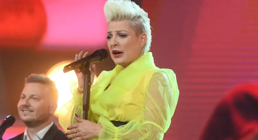 Wokalistka w neonowej kreacji śpiewa canzone d'amore, a obok niej mężczyzna z uśmiechem na twarzy.