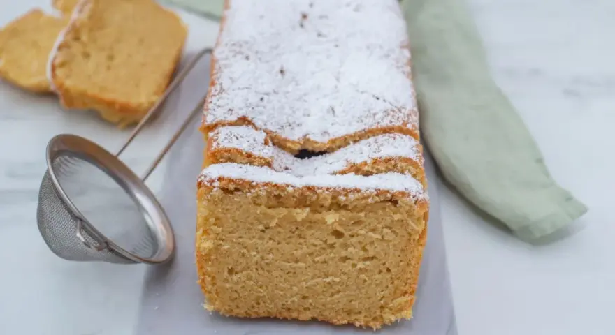 Puszyste keto ciasto z mikrofali, posypane cukrem pudrem, prezentuje się apetycznie. Obok leżą dwa kawałki ciasta i sitko.