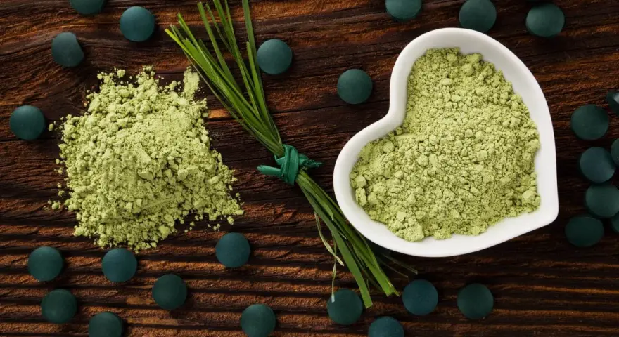 Zielony proszek i tabletki na drewnianym tle. Dowiedz się, spirulina co to za superfood!