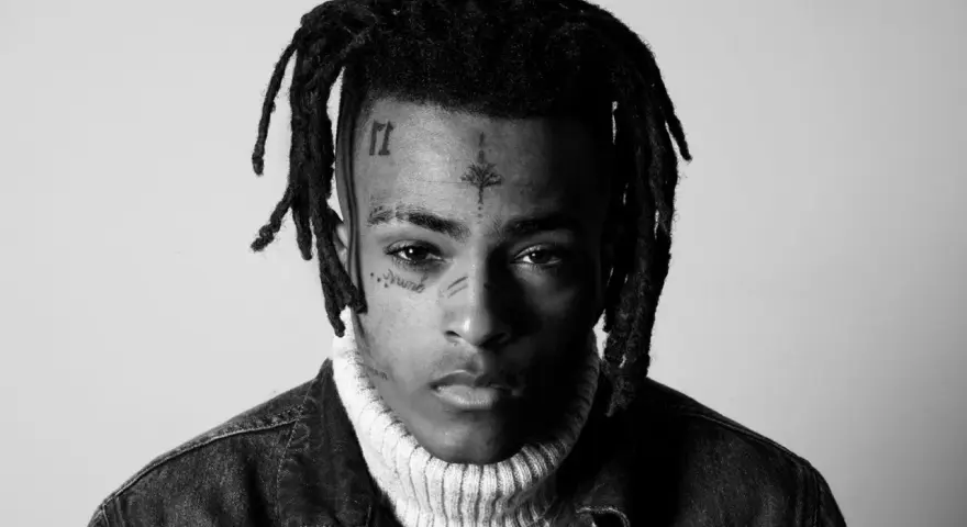 Czarno-białe zdjęcie rapera z tatuażami na twarzy, w golfie i kurtce dżinsowej. Wiele osób wspominało go, kiedy umarł xxxtentacion.