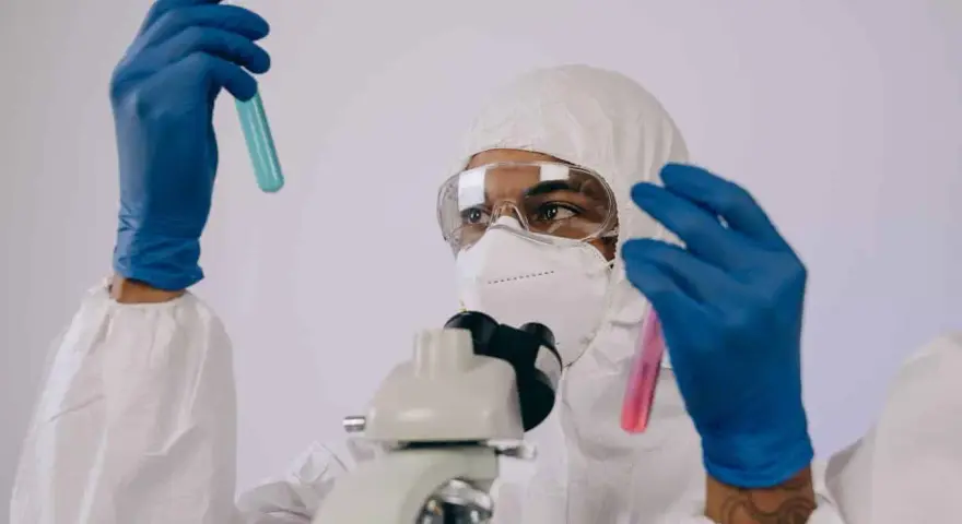 Badacz w kombinezonie i masce analizuje próbki w probówkach, przygotowując się do pracy w laboratorium chemicznym.