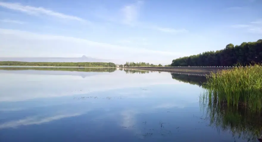 Spokojny zalew Dziećkowice z odbijającymi się w tafli wody chmurami i zielonym lasem w tle.