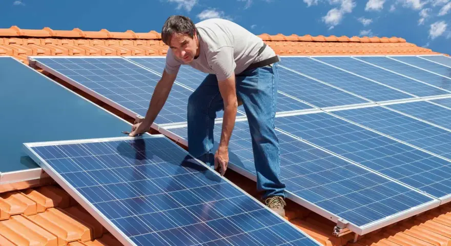 Instalator montuje panele fotowoltaiczne na dachu. Pokazuje, jak zamontować panele fotowoltaiczne, by czerpać energię ze słońca.