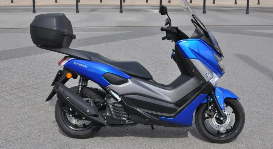 Niebieski skuter Yamaha NMAX 125 z kufrem, gotowy do jazdy. Jego prędkość maksymalna pozwoli na szybkie przemieszczanie się po mieście.