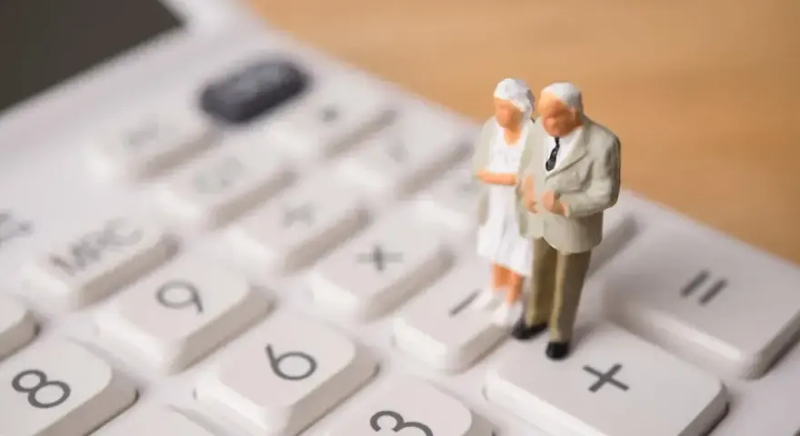 Figurki starszej pary na kalkulatorze symbolizują planowanie przyszłości i obliczanie emerytury stażowej.