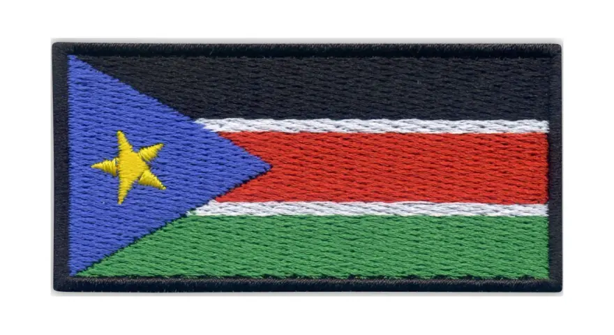 Naszywka z flagą Sudanu Południowego. Czarny pas na górze, pod nim biały, czerwony i zielony pas. Z lewej strony niebieski trójkąt z żółtą gwiazdą.