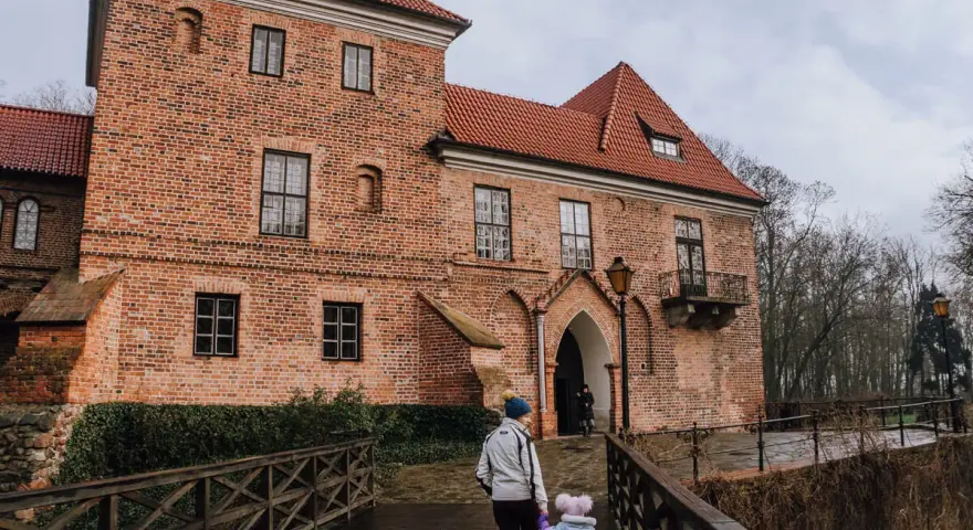 Rodzina idzie drewnianym mostkiem do ceglanego zamku w Oporowie.