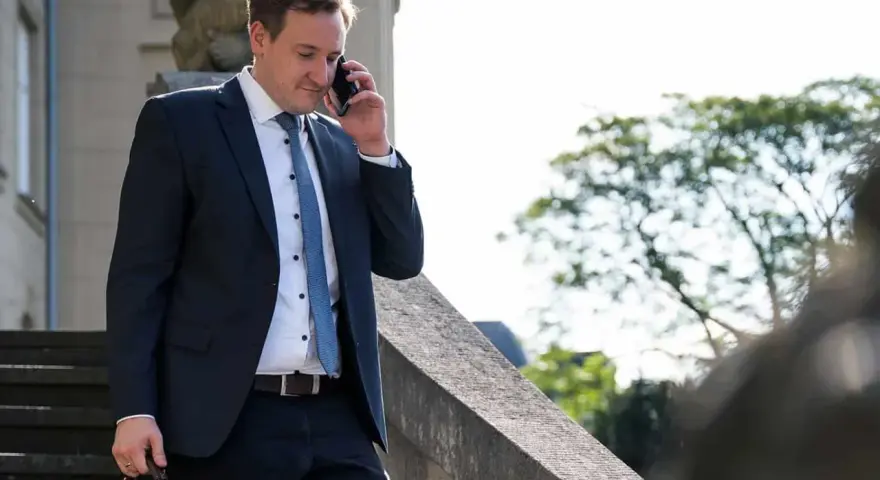 Anwalt am Telefon, der überlegt, wie kann ich mich schnell scheiden lassen. Er trägt einen dunklen Anzug und hält eine Aktentasche.