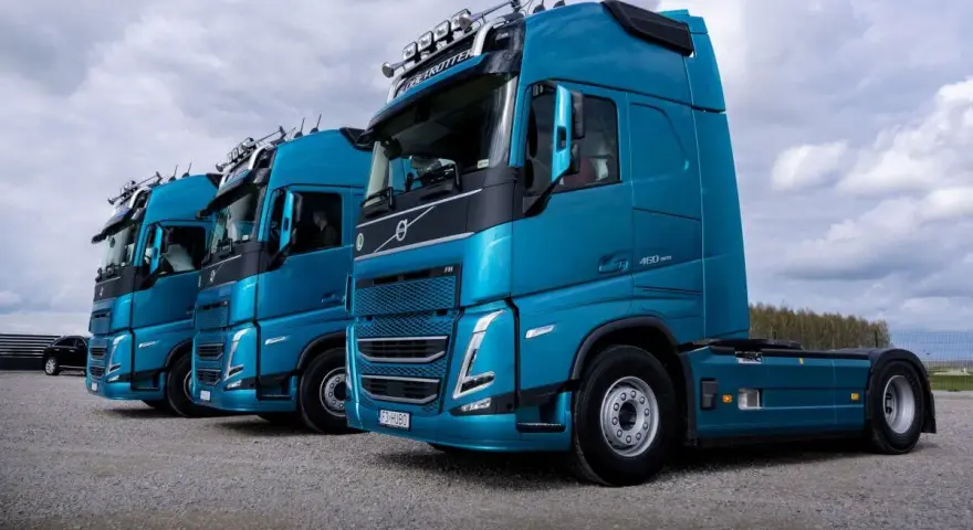 Rząd lśniących, turkusowych ciężarówek Volvo FH gotowych do transportu żywności.