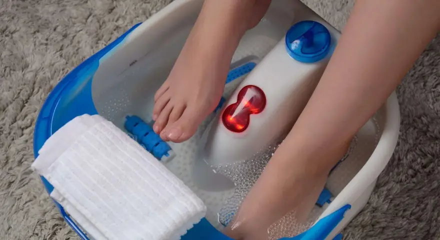 Pieds dans un bain à bulles, profitant d'un moment de détente pour la beauté des pieds. Une serviette blanche est à portée de main.