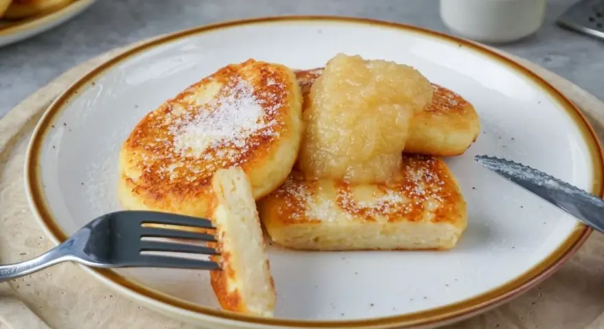 Goldbraune Quarkkeulchen, bestreut mit Zucker, serviert mit Apfelmus. Ein leckeres Quarkkeulchen Rezept zum Genießen.