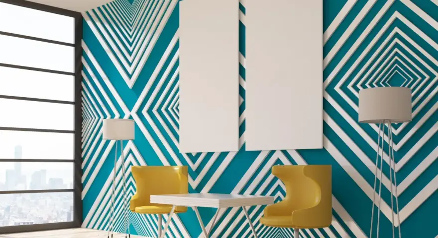 Modern room with striking **diseños pared geometrica** in teal and white. Two yellow chairs and a table sit before the wall, with floor lamps and blank canvases.