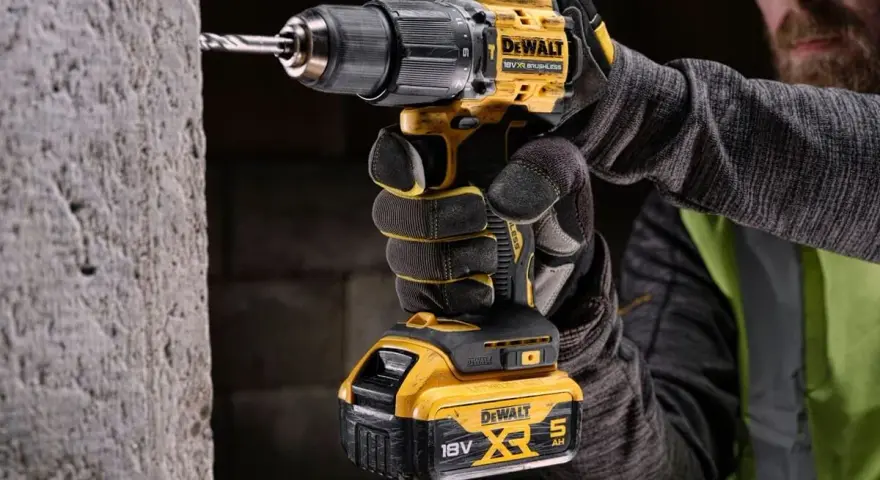 Mężczyzna w rękawicach wierci w betonie najmocniejszą wkrętarką DeWalt 18V XR.