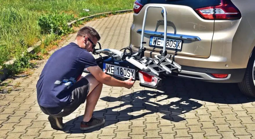 Mężczyzna montuje tablicę rejestracyjną na bagażniku rowerowym, by uniknąć mandatu za brak tablicy rejestracyjnej na bagażniku rowerowym.