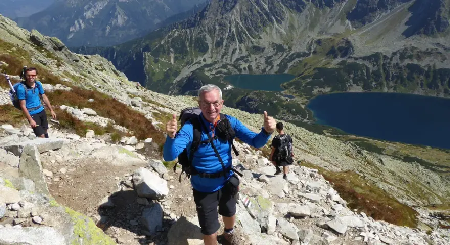 Trasa na Kozi Wierch. Dwóch turystów z plecakami na skalistym szlaku, w tle piękne tatrzańskie jeziora.