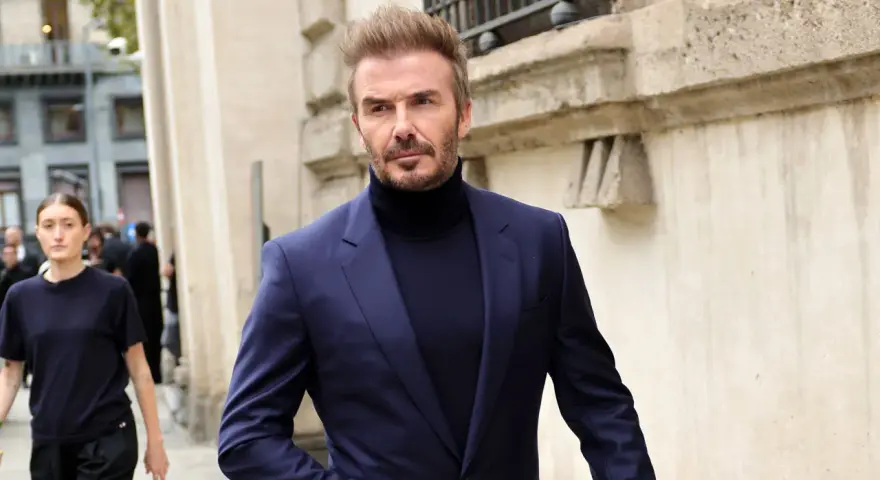 David Beckham luce un elegante traje azul con jersey de cuello alto, caminando con confianza.