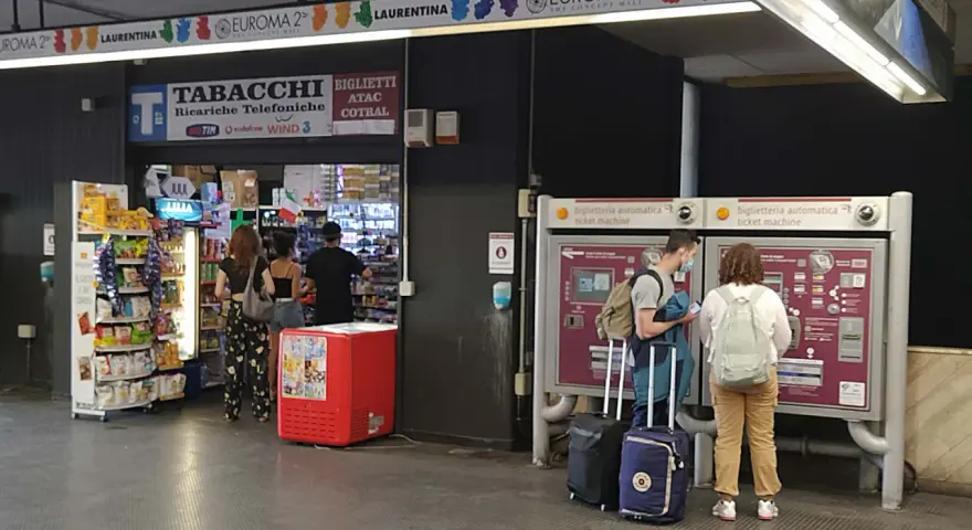 Na dworcu w Rzymie Ciampino ludzie kupują bilety i artykuły w sklepie.