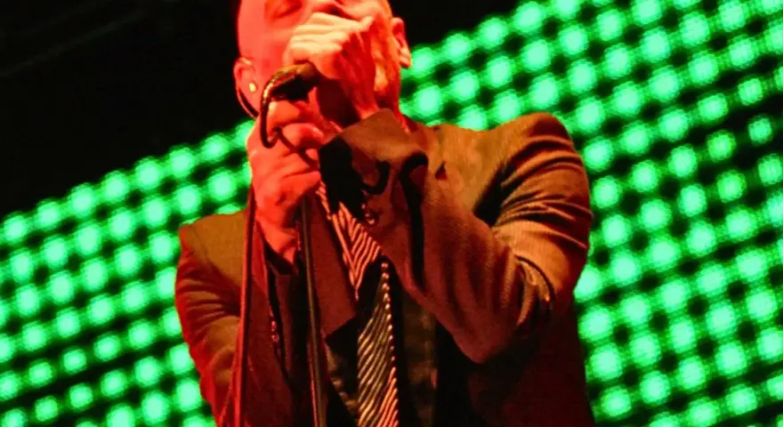 Wokalista REM, Michael Stipe, śpiewa na scenie, gdy światła migoczą na zielono.