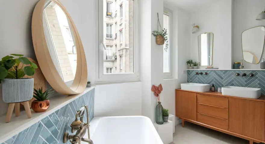 Salle de bain moderne avec carrelage zellige bleu canard, baignoire, double vasque sur meuble vintage et miroir rond en bois. Inspiration zellige.