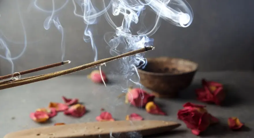 Humo de incienso de lavanda asciende, evocando paz y el significado espiritual de la calma. Pétalos secos y un cuenco completan la escena.