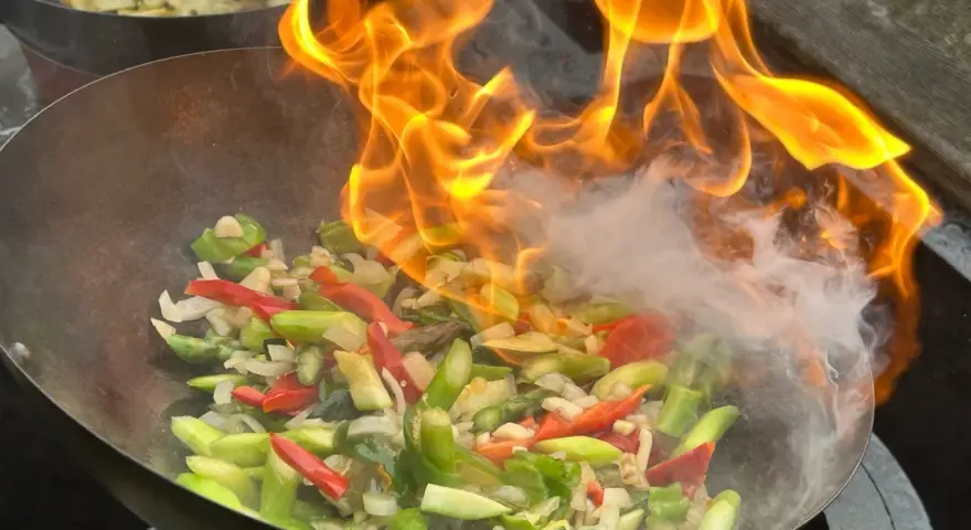 Ogień płonie w woku, przygotowując warzywa do stir fry. To szybkie smażenie, które zachowuje świeżość składników.