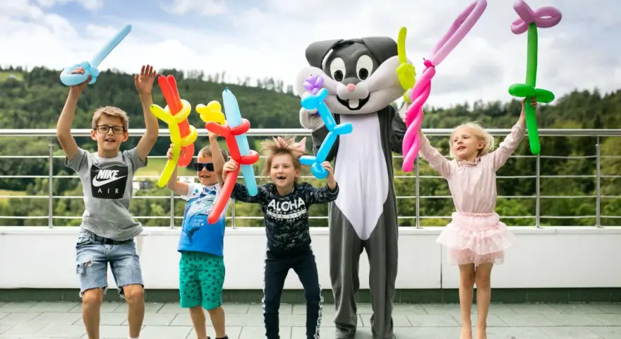 Radosne dzieci z balonami w kształcie zwierzątek i mieczy świętują koniec roku szkolnego z postacią królika.