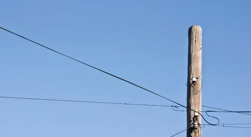 Słup energetyczny z przewodami, symbolizujący zgodę na światłowód nad działką.