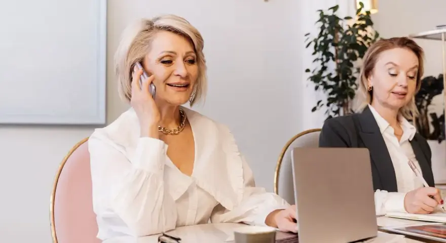 Dwie kobiety w biurze, jedna rozmawia przez telefon, druga pisze.