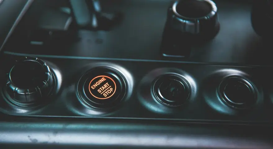 Podświetlany przycisk "ENGINE START STOP" w samochodzie. Obok niego pokrętło wyboru trybu jazdy, jak czujnik IBS.